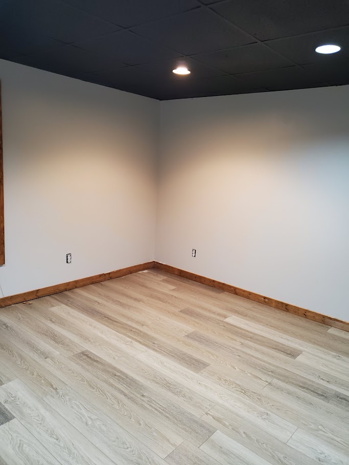 Finished interior room with light neutral painted walls, contrasting black ceiling tiles, and wood baseboards.