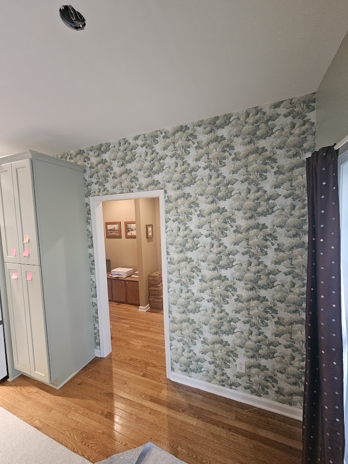 Floral wallpaper installation featuring blue and green botanical patterns, white trim, and wood flooring.