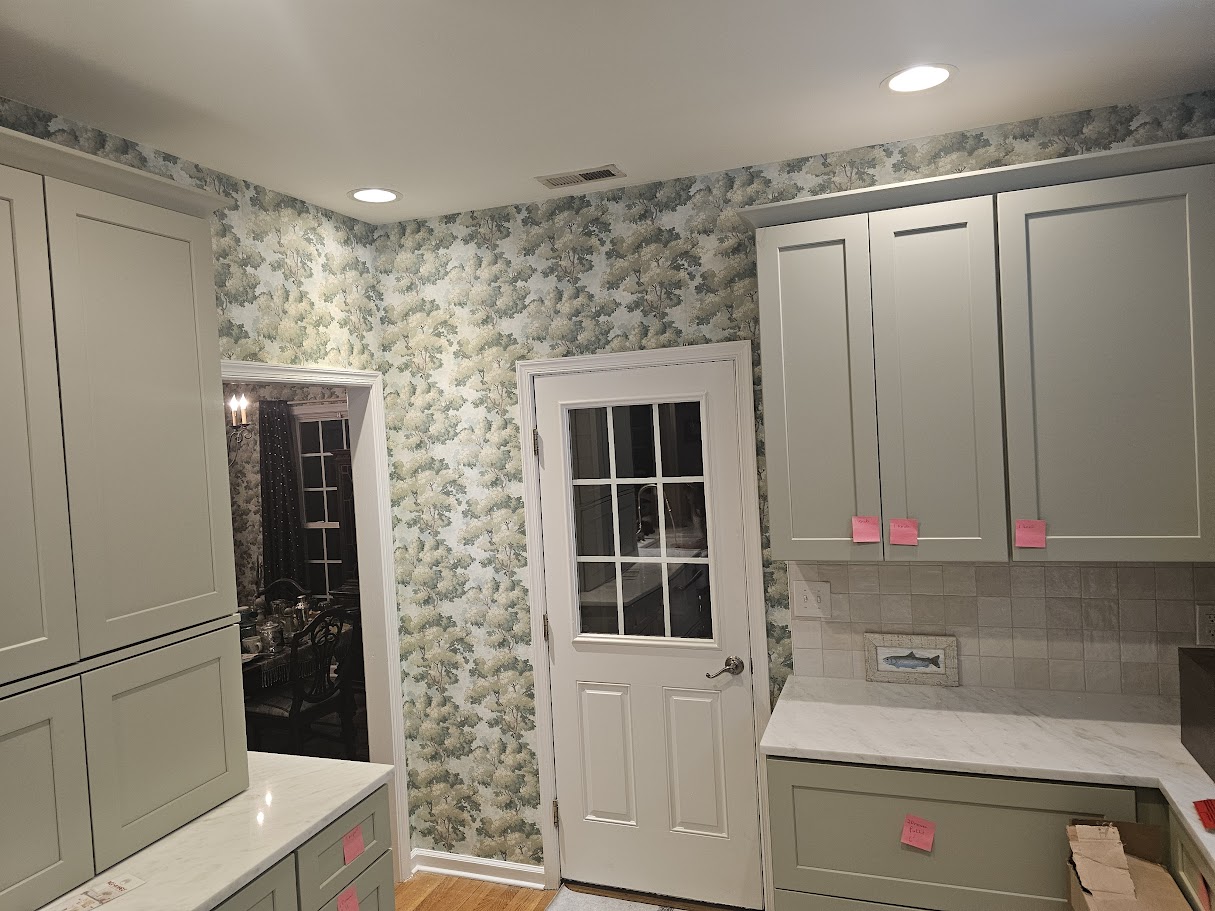Kitchen wall covering featuring blue and green botanical-patterned wallpaper around a white door and cabinetry.