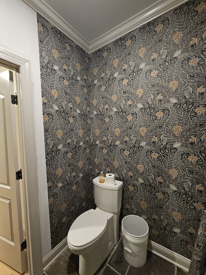 Bathroom featuring dark floral wallpaper with gold accents, white crown molding, and decorative wall coverings.